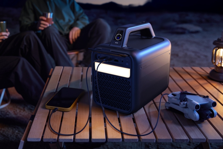 The Anker Nebula Mars 3 outdoor projector with its LED light on and devices charging off of it.
