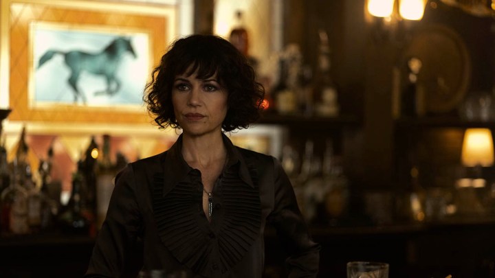 Carla Gugino as Verna standing behind a bar and looking intently off-camera in The Fall of the House of Usher.